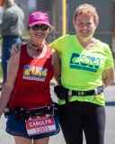 Two runners with their arms around each other and smile towards the camera.