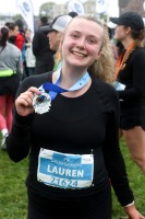 A runner smiles at the camera while holding up their medal.