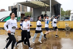 A group of runners in matching black and white clothing smile as they run with one person's arms in the air and another waving