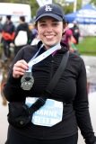 A runner smiles at the camera while holding up their medal.