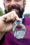 A close up of a man’s hand holding their medal with their face in the background.