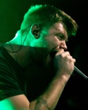 A punk rock singer screams into the microphone lit with saturated green light