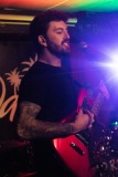 A guitarist strums and sings with a bright lens flare.