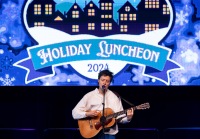 A person on stage with a guitar singing into the microphone with a banner behind them
