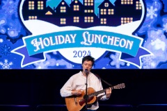 A person on stage with a guitar singing into the microphone with a banner behind them