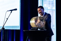 An MC smiles as they are about to get a prize winning raffle ticket from the pot