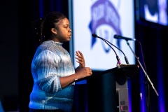 A person gestures to the crowd at the podium