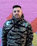 A man poses for a portrait with a small portion of their colourful mural behind them.