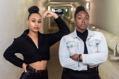 Two women pose and look at the camera together with one woman's arm on the other's shoulder.