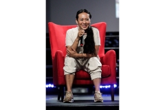 A woman smiles while sitting in a red chair on stage