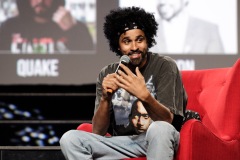 A man speaks on stage while sitting in a red chair