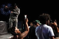 A woman takes a photo while a man on stage dances and people in the crowd mingle