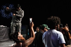 A woman takes a photo while a man on stage dances and people in the crowd mingle