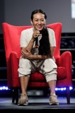 A woman smiles while sitting in a red chair on stage
