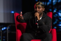 A man gestures while speaking and sits on a red chair