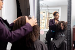 A woman and her smiling client is reflected in a mirror adjusting the sitting woman's hair