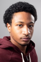 A man looks directly into the camera in front of a plain background.